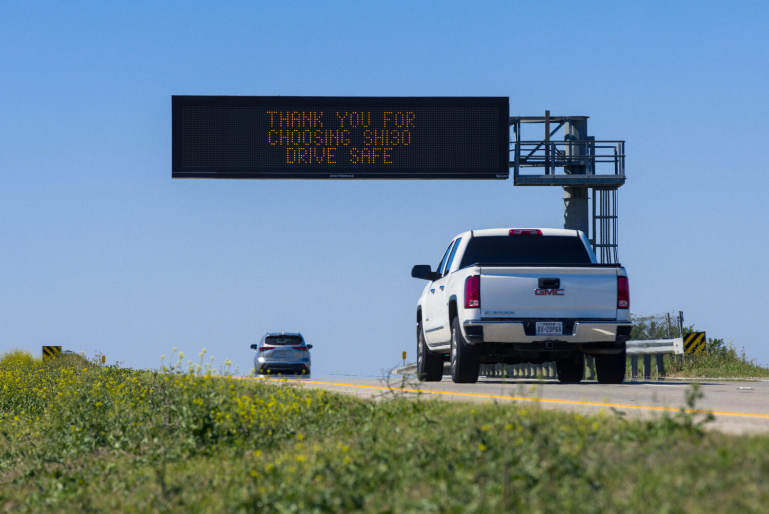 Cars on SH 130 in Texas with a road sign thanking drivers for taking the road and urging them to drive safely.
