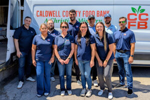SH 130 staff members posing together in front of a Caldwell County Food Bank van during a volunteer event.