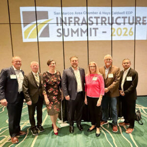 A group of seven attendees posing in front of the San Marcos Area Chamber & Hays Caldwell EDP Infrastructure Summit 2026 banner.