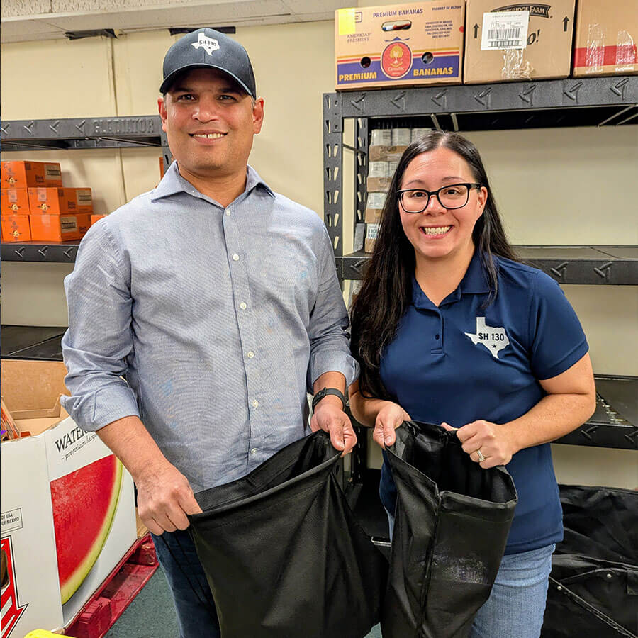 Two SH 130 staff members holding donation bags inside the Caldwell County Food Bank during a volunteer visit.