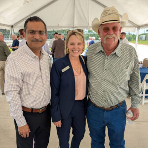 Three community members posing together under a tent at an outdoor SH 130 event.