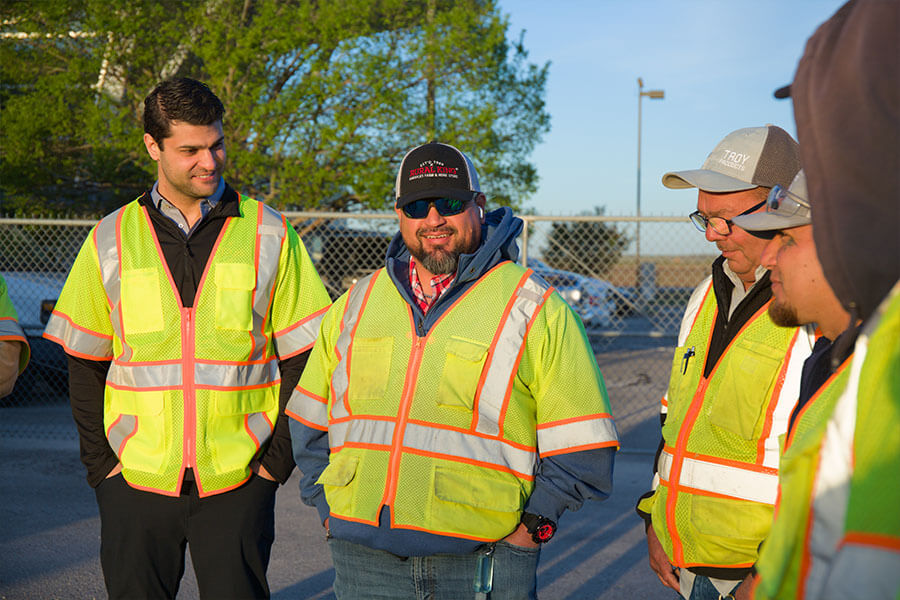 SH 130 crew members in high-visibility safety vests talking together outdoors at an SH 130 facility.