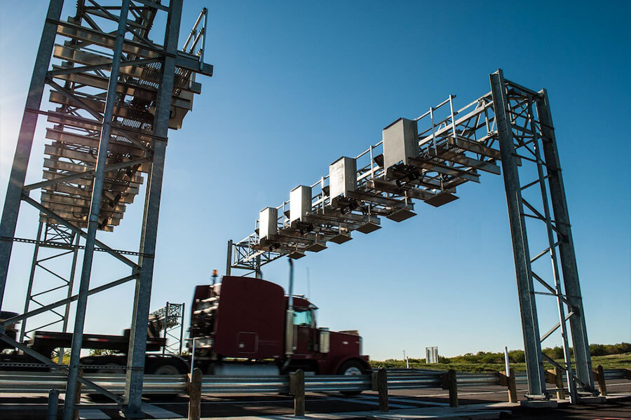 A commercial truck passing under an SH 130 electronic toll gantry on a clear day.
